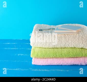 three multi-colored new terry bath towels folded on a blue wooden background and empty paper business cards Stock Photo
