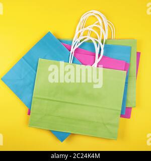 stack rectangular multi-colored paper shopping bags with white handles on a yellow background, flat lay Stock Photo