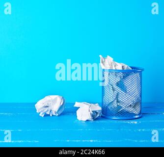 blue metal bucket filled with crumpled white paper, blue background, business concept Stock Photo