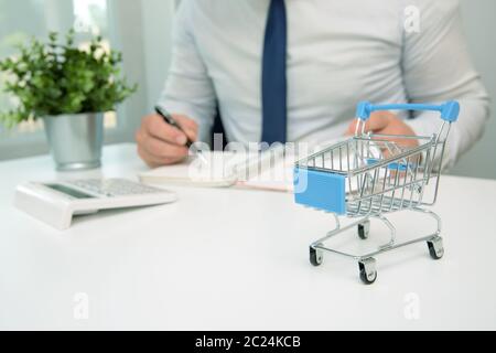Businessman calculating shopping expenses, holding receipts in hand. Empty shopping cart in front. Home finances, investment, economy, saving money co