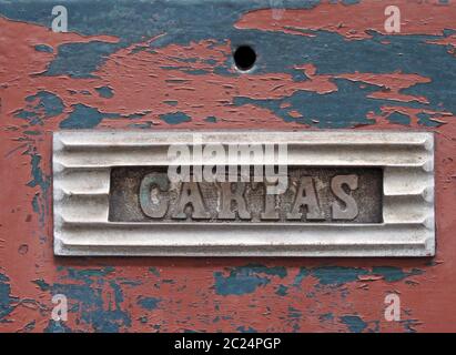 an old metal letterbox in a red wooden door with chipped peeling paint with the word cartas, translation from portuguese is mail Stock Photo