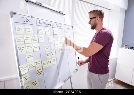 Smiling Businessman Sticking Adhesive Note On White Board In Office Stock Photo