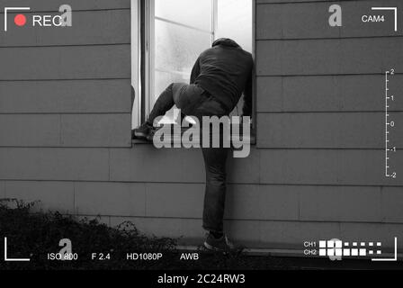 Rear View Of A Burglar Entering In A House Through A Open Window Stock Photo