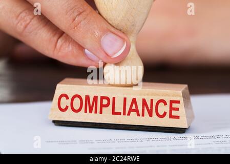 Close-up Of A Businessperson's Hand Stamping Compliance On Paper In Office Stock Photo