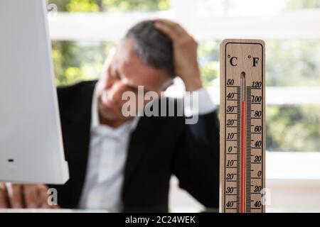 Thermometer In Front Of Businessman Working During Hot Weather In The Office Stock Photo