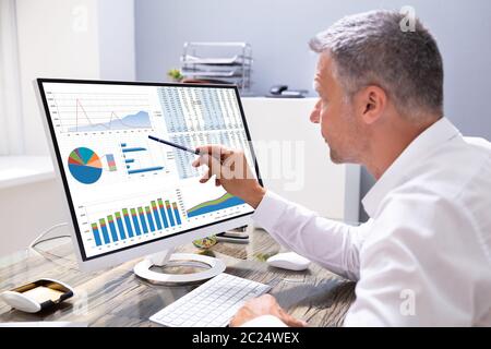 Businessman Analyzing Graphs On Computer At Workplace Stock Photo