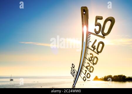 Background for a hot summer day or a heat wave, beach with people, bright sun and a big thermometer Stock Photo