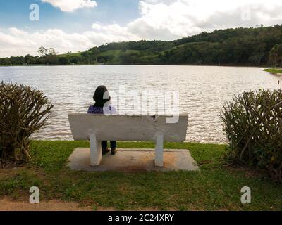 Unrecognized girl sitted in a seat in front of a lake in backlight Stock Photo