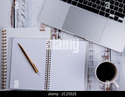 A wooden white table with a computer and empty notebooks on which lies a pen and a cup of coffee nearby stands. High quality photo Stock Photo