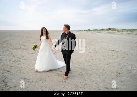 Wedding couple walking on sandy beach. Bride and groom looking to each other and smiling. Barefoot husband. Wedding day concept. Stock Photo