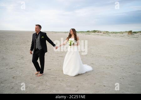 Wedding couple walking on sandy beach. Barefoot bride and groom. Wedding day concept. Stock Photo