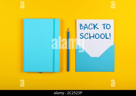 Back to school handwritten sign on white paper in blue envelope next to leather cover notebook over yellow paper background with copy space Stock Photo