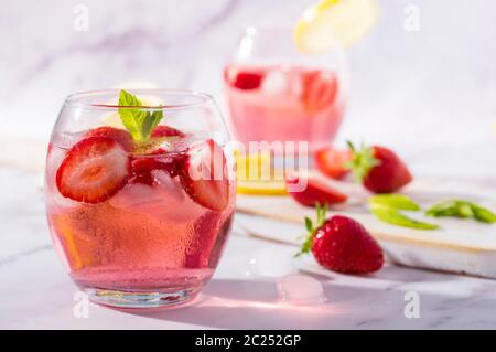 Cold pink strawberry flavoured gin and tonic garnished with fresh fruits, lemon and mint leaves. Stock Photo