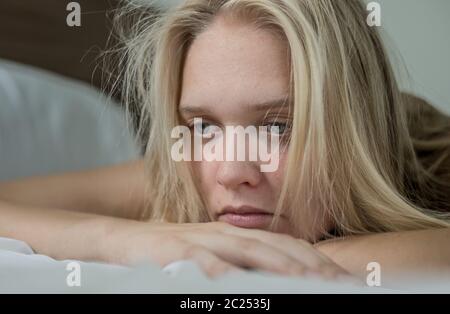 A unhappy woman with a sad expression on her face lying in bed at home. Stock Photo