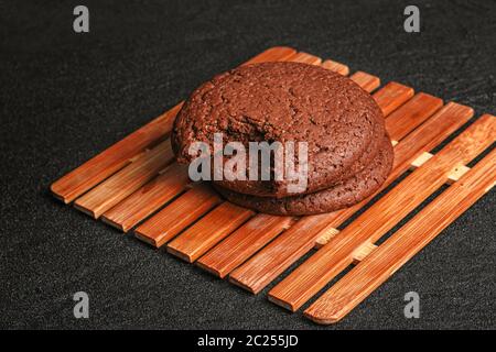 chocolate oatmeal cookies three pieces one bitten lies on a bamboo plate on black concrete Stock Photo