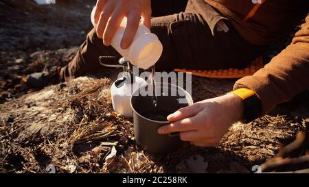 Hands man Close-up pours water from flasks into a pot for boiling water on a gas tourist burner camping forest Stock Photo