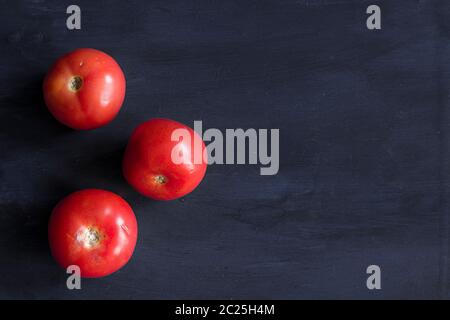 Three tomatoes on a dark blue table. Healthy vegetables Stock Photo