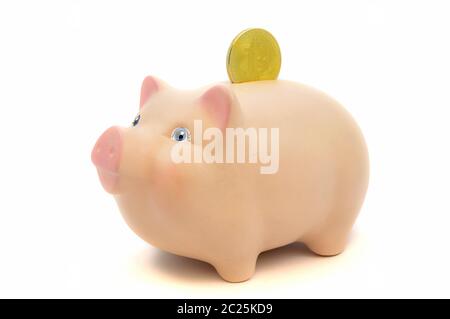 A closeup image of a golden Bitcoin piece being deposited into a piggy bank for concepts related to the cryptocurrency business. Stock Photo