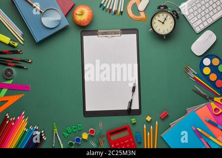 Black clipboard with blank sheet, computer keyboard, calculator and stationery accessories  on green background. Top view, copy space. School accessor Stock Photo