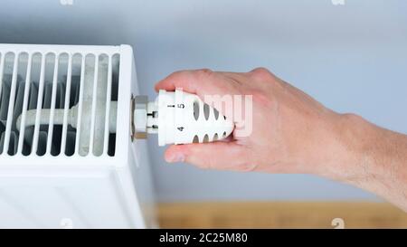 Hand adjusting thermostat valve of heating radiator in a room. Stock Photo