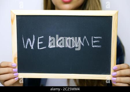 Welcome written on the blackboard holding by young unidentified woman.