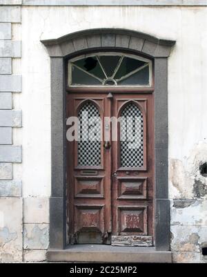 an old ornate brown double house door with broken repaired panels and hand shaped knocker with stone frame and doorstep Stock Photo