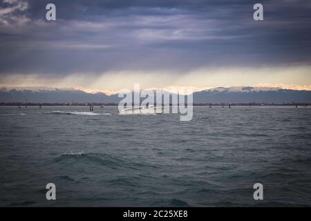 View of Venice Lagoon with dramatic overcast stormy sky and horizon in the distance sunlit peaks of Dolomite Alps, Venice, Italy Stock Photo