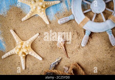 Sandy beach old blue wood background on decorative steering wheel with starfish, seashells Stock Photo