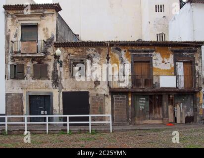 a row of derelict abandoned houses and commercial properties on a street with boarded up doors and windows and crumbling walls Stock Photo