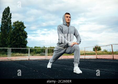 Handsome sportsman doing exercises for legs, lunges, dressed in sportswear, outdoors Stock Photo