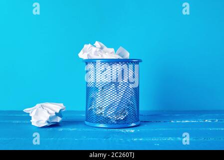 blue metal bucket filled with crumpled white paper, blue background, business concept Stock Photo