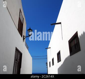 street of traditional white houses in perspective view looking upwards with bright blue summer sky leading to the sea Stock Photo