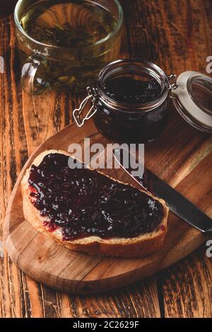 Toast with berry jam on cutting board and cup of green tea in rustic setting Stock Photo