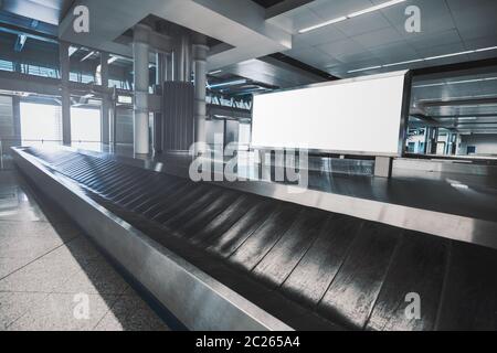 A white blank rectangular advertising billboard mock-up in airport baggage claim hall with a conveyor in front; advert poster template indoors Stock Photo