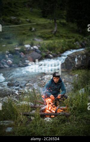 Young man making fire while camping outdoors, in an alpine wilderness Stock Photo