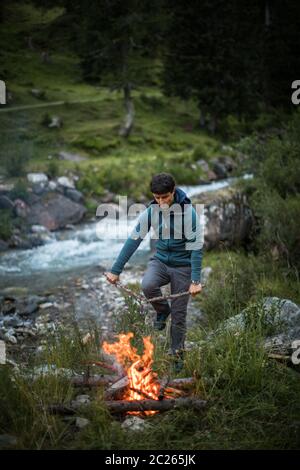 Young man making fire while camping outdoors, in an alpine wilderness Stock Photo