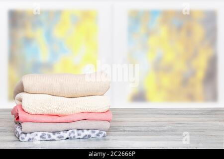 Stack of winter clothes. Pile of colorful knitted cozy warm sweaters or pullover on wooden table against blurred bright autumn background. Space for d Stock Photo