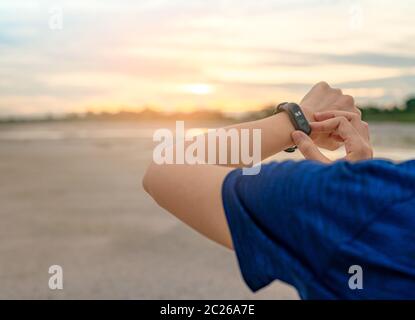 Young Asian woman touching smart band after running in the morning. Wearable computer. Heart rate monitor bracelet. Fitness device. Activity or fitnes Stock Photo