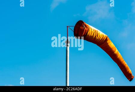 Orange windsock in moderate wind on white pole against clear blue sky on sunny day at aviation area. Wind direction sign at the airport field Stock Photo