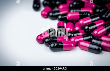 Pink-black capsule pills on white table. Antibiotics drug resistance. Global healthcare. Antimicrobial capsule pills. Pharmacy background. Antibiotic Stock Photo