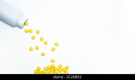 Yellow film coated tablets pills spilling out of pill bottle on white background with copy space. Painkiller tablet pills. NSAIDs pills for muscle pai Stock Photo