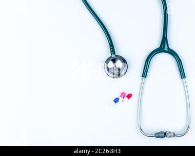Top view of green stethoscope with pile of antibiotic capsule pills on white table. Antimicrobial drug resistance and overuse. Medical equipment for d Stock Photo