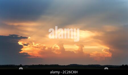 An orange sunset as the sun rays burst through passing storm clouds. Stock Photo