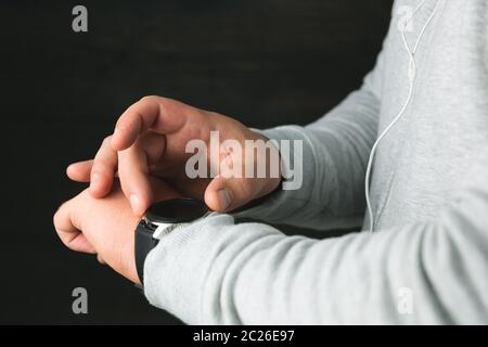 Man in a sport hoodie checking notification on digital smartwatch display. Man's hands with wearable computer wrist watch Stock Photo