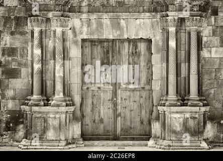 monochrome sepia ancient wooden double doors in an old stone building with crumbling ornate columns surrounding the entrance Stock Photo