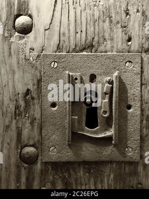 a sepia monochome large square rusty iron lock with keyhole in an old wooden door and metal rivets Stock Photo