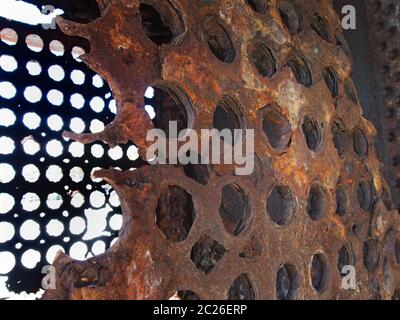 rusted decaying iron panels covered in round holes with light shining though on obsolete heavy machinery Stock Photo