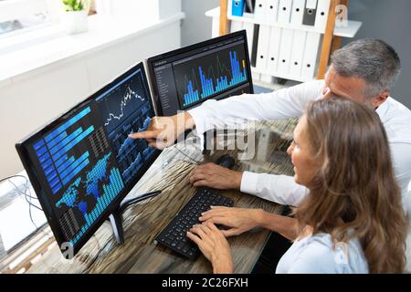 Side View Of Male And Female Stock Market Broker Analyzing Graphs On Laptop At Workplace Stock Photo