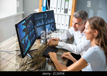 Side View Of Male And Female Stock Market Broker Analyzing Graphs On Laptop At Workplace Stock Photo