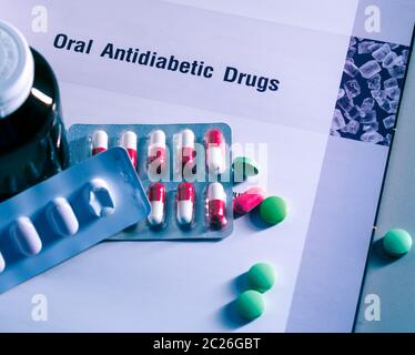 Diabetes drugs in packs and and medicine bottle placed on textbook. Green tablets and pink-white capsule pills. Diabetes mellitus therapy concept. Stock Photo